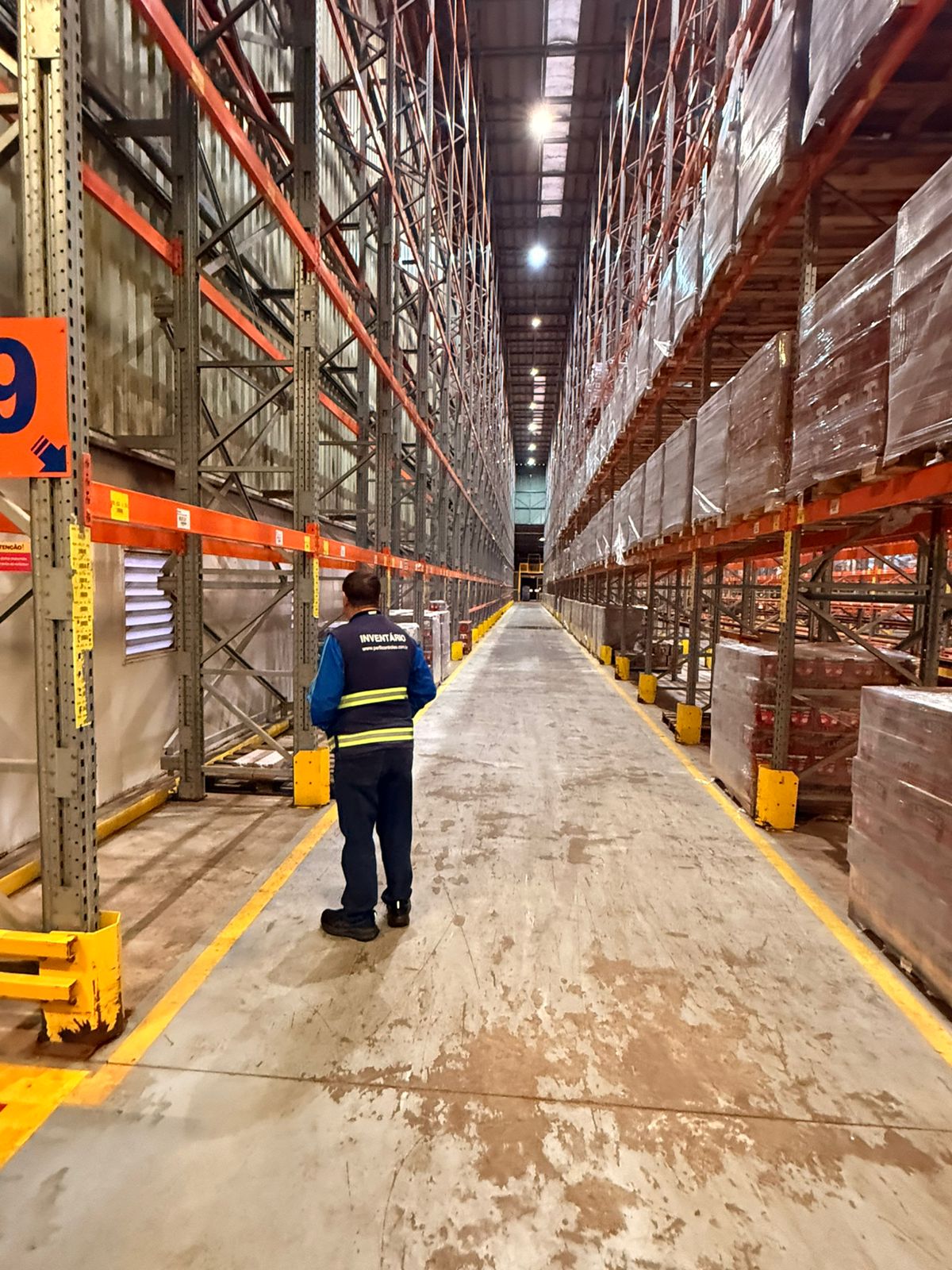 Técnico da Perfil em operação de campo, conferindo estoque em corredor de porta-pallets industrial.